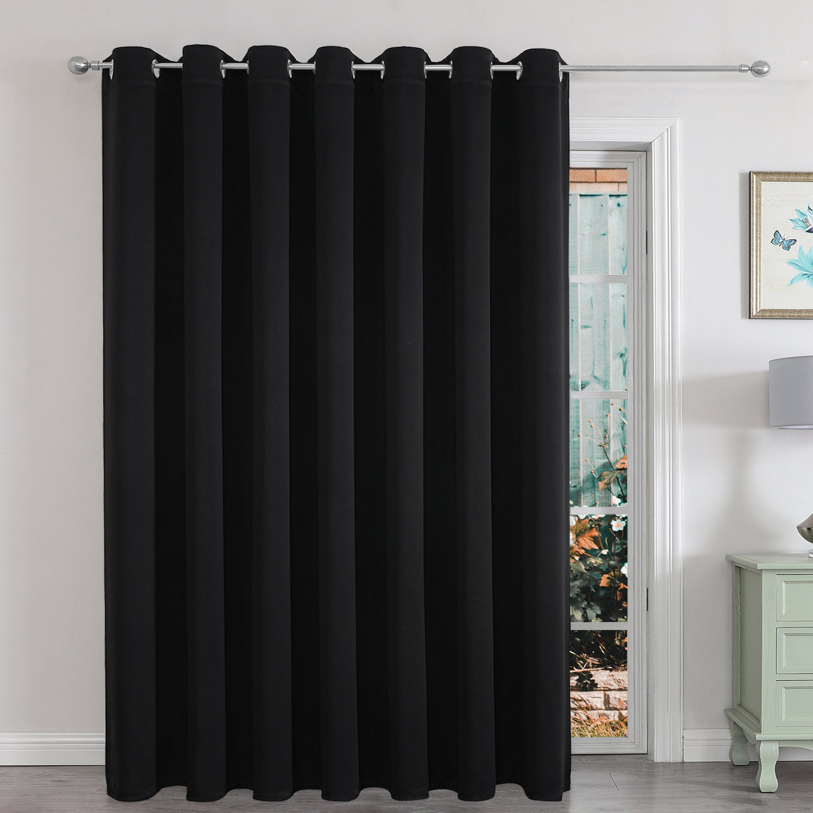 Black extra-wide blackout curtain panel for sliding glass door in a living room, providing privacy and light control.