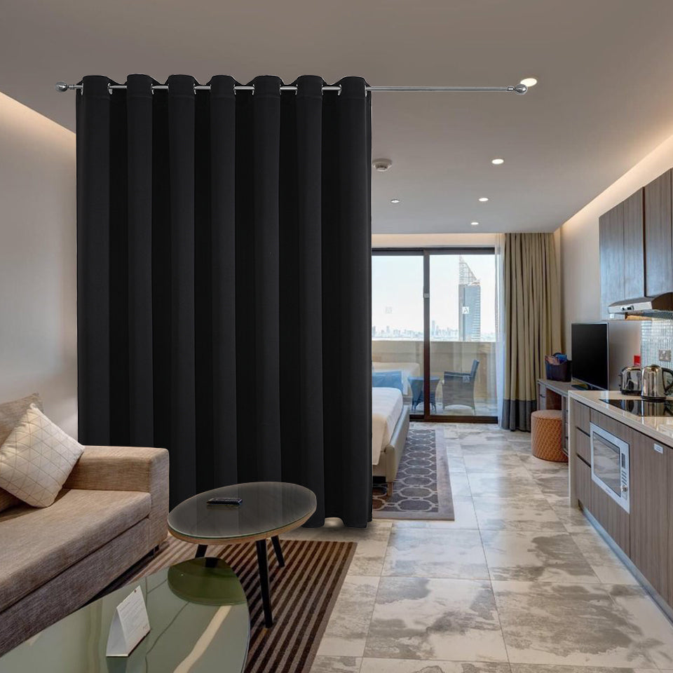 Black extra wide blackout room divider curtains installed in a studio apartment, separating living area from bedroom.