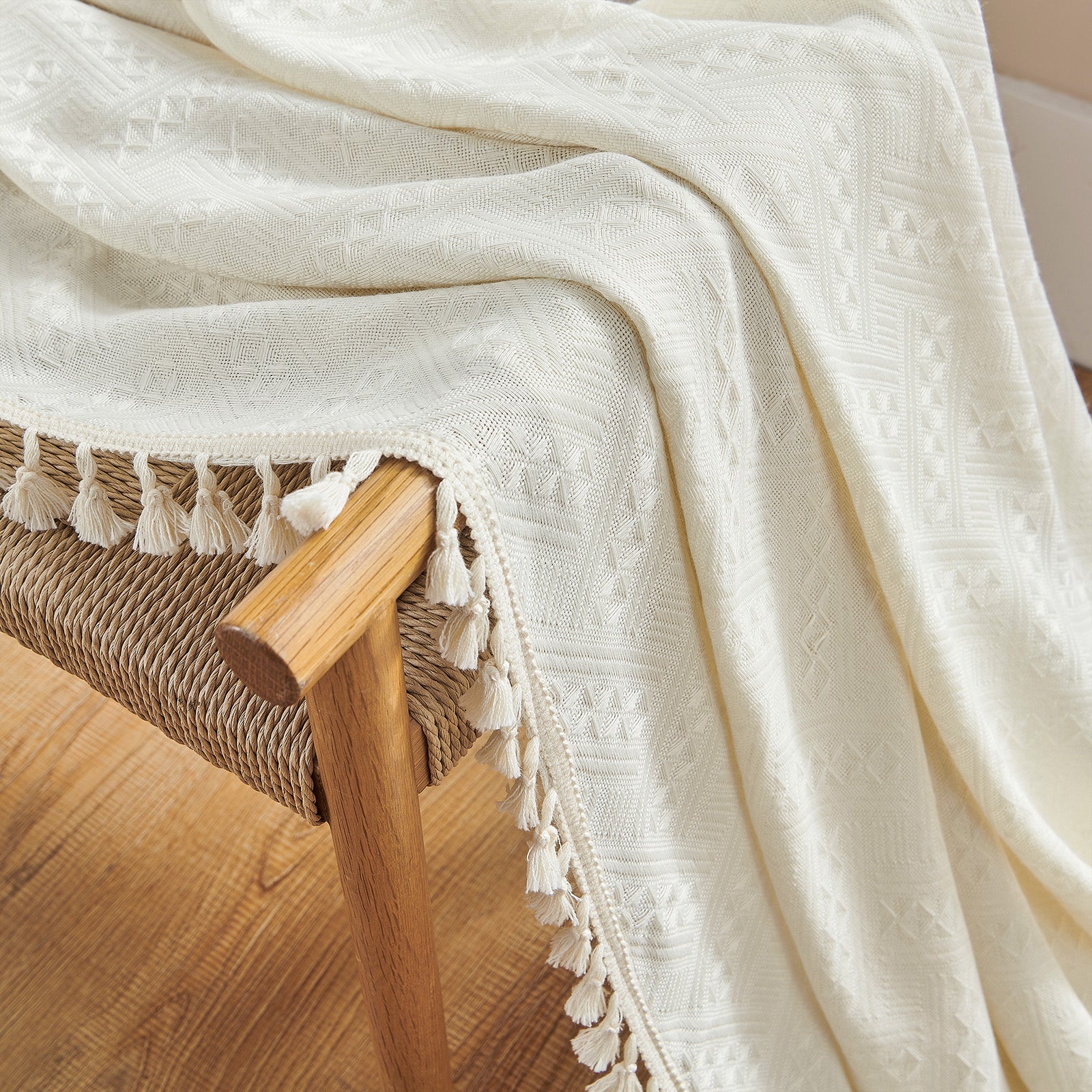 Close-up texture of Joydeco cream boho curtains featuring diamond pattern and cream tassels, draped over a woven chair.