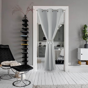 Light grey extra-wide room divider curtain with silver grommets and tassel tie-back, separating living room from kitchen.