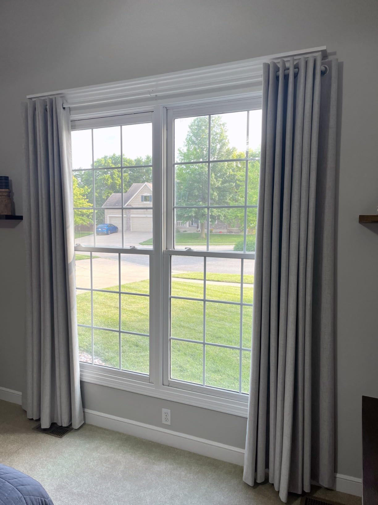Joydeco light gray grommet blackout curtains hanging on a white rod in a multi-pane window, showcasing room integration.