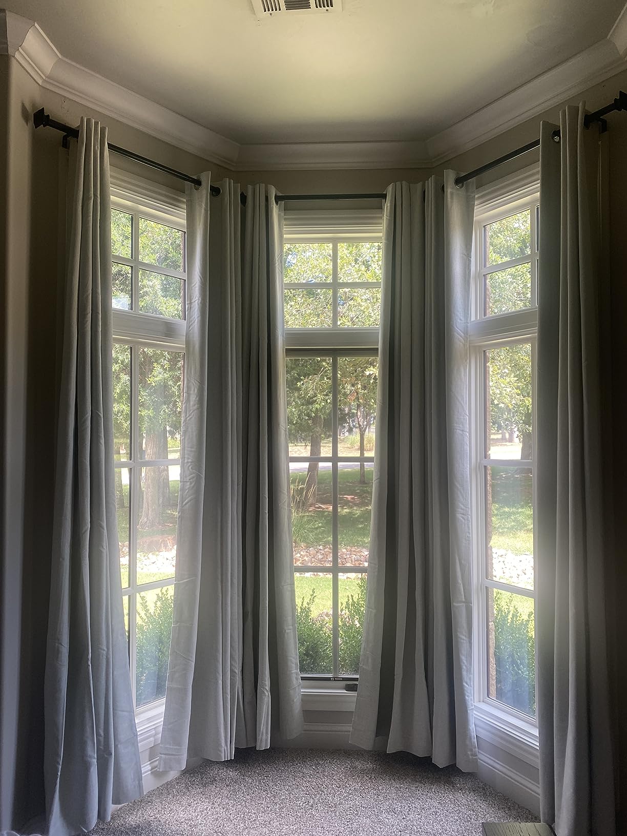 Light gray Joydeco blackout curtains hanging on dark rods in a bay window, showing drape and room setting.