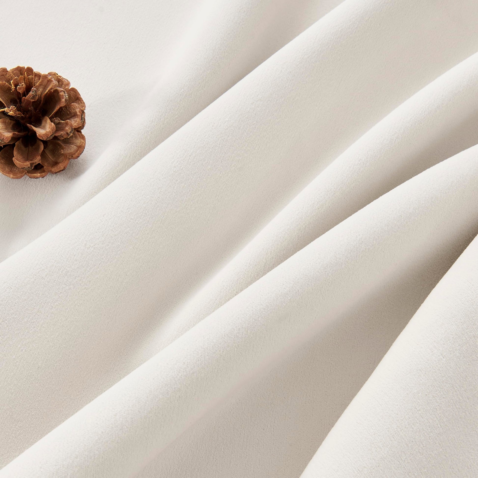 Cream velvet fabric texture close-up with pinecone, highlighting luxury blackout and thermal drapes.