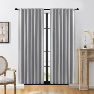Two light gray Joydeco blackout curtains with vertical pleats on a black rod in a living room.