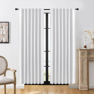 Joydeco white 100% blackout curtains with soft brushed texture and vertical pleats on a black rod in a living room.