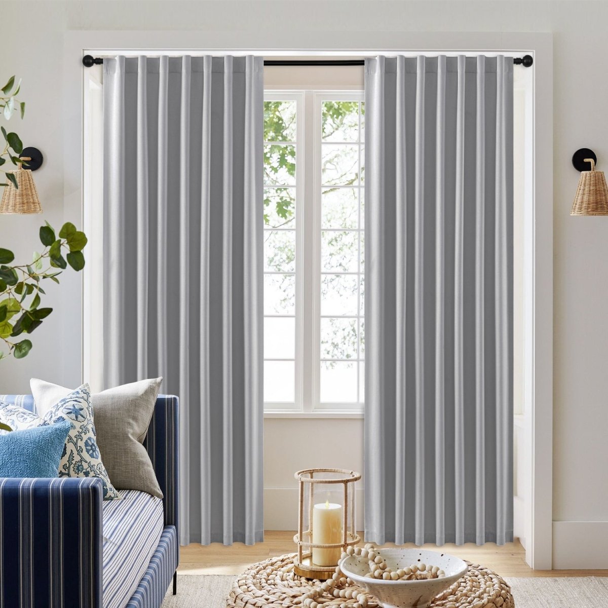 Two light gray Joydeco blackout curtains with soft vertical pleats hanging from a black rod in a living room.
