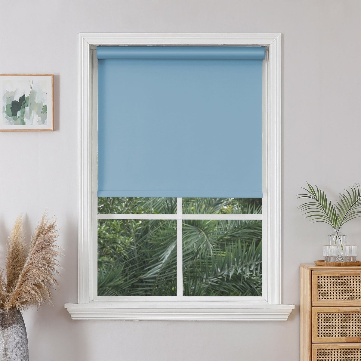 Light blue Joydeco cordless blackout roller shade partially lowered in white window, showing greenery outside.