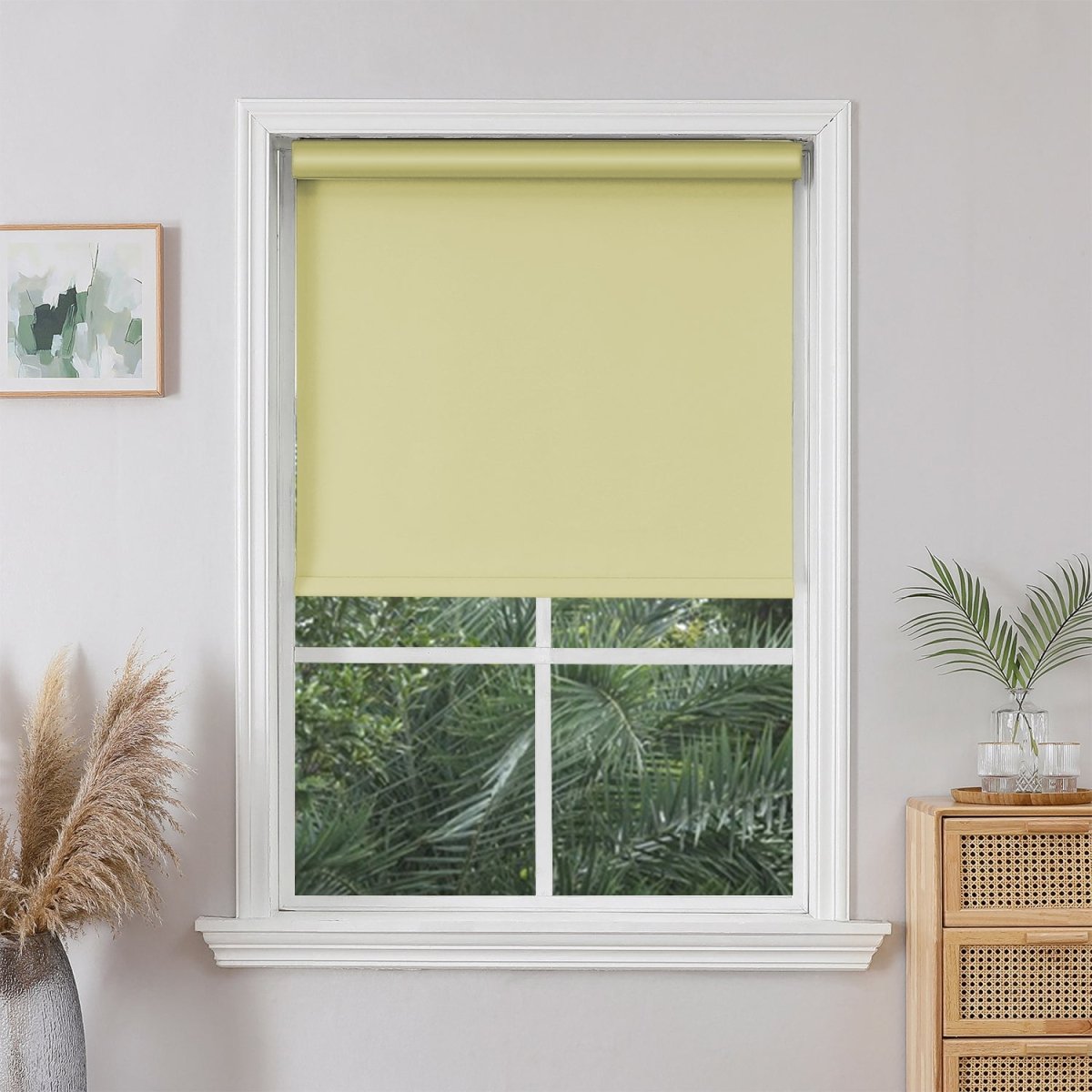 Light yellow Joydeco cordless blackout roller shade installed in a white window frame, providing full light blockage.
