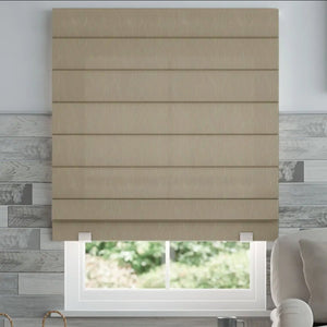 Joydeco beige textured woven Roman shade with horizontal pleats, shown on a window with a view of greenery. Armchair visible.