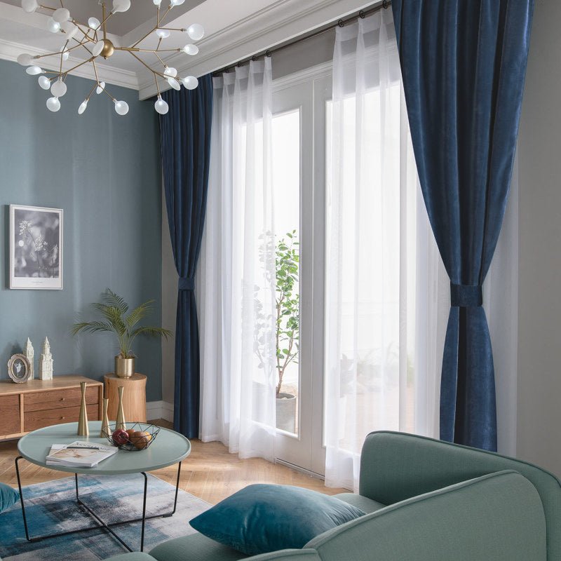 Custom deep navy blue velvet blackout curtains layered with sheer white, enhancing room ambiance.