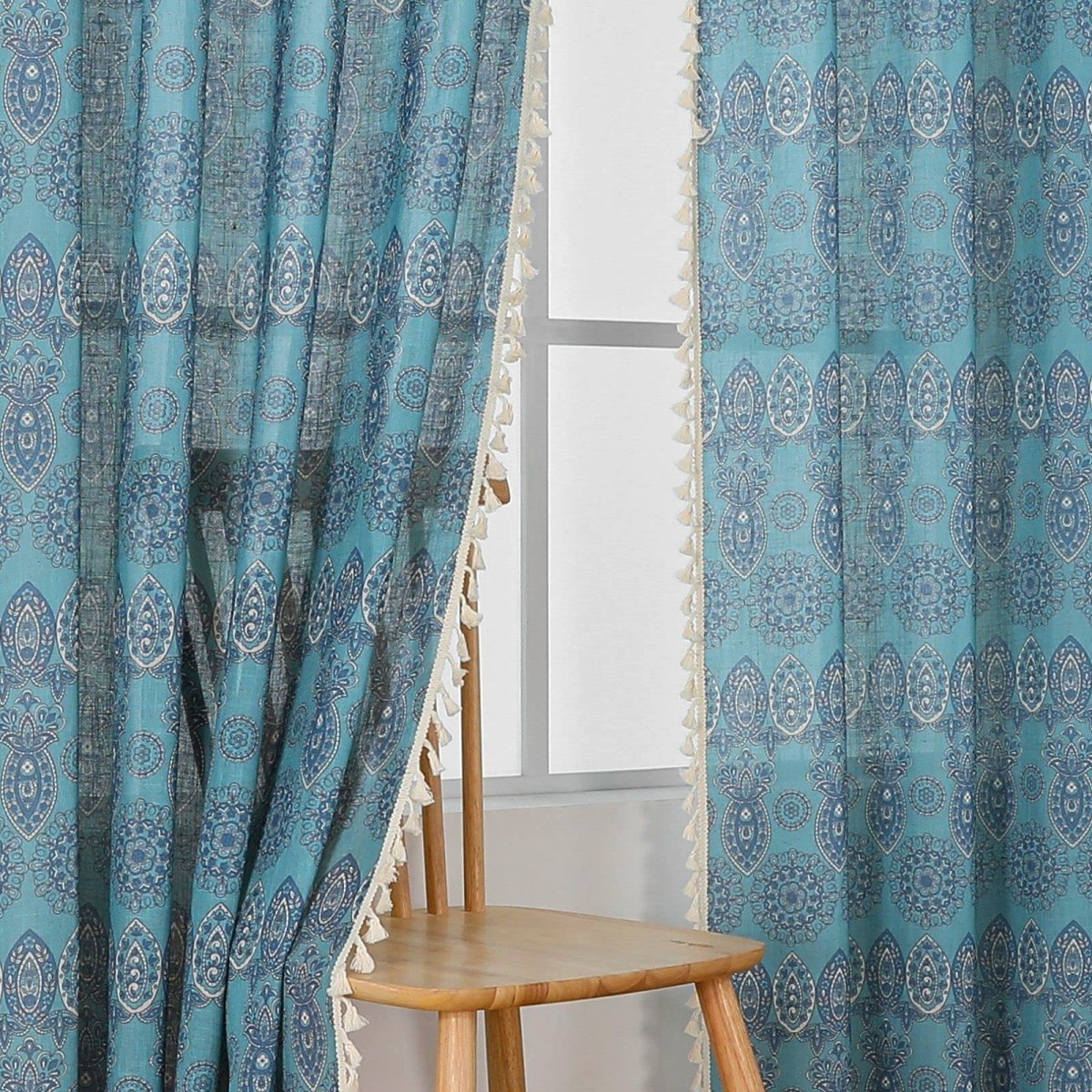 Turquoise bohemian curtains with intricate blue medallion and paisley patterns, cream tassel trim. Light filtering.