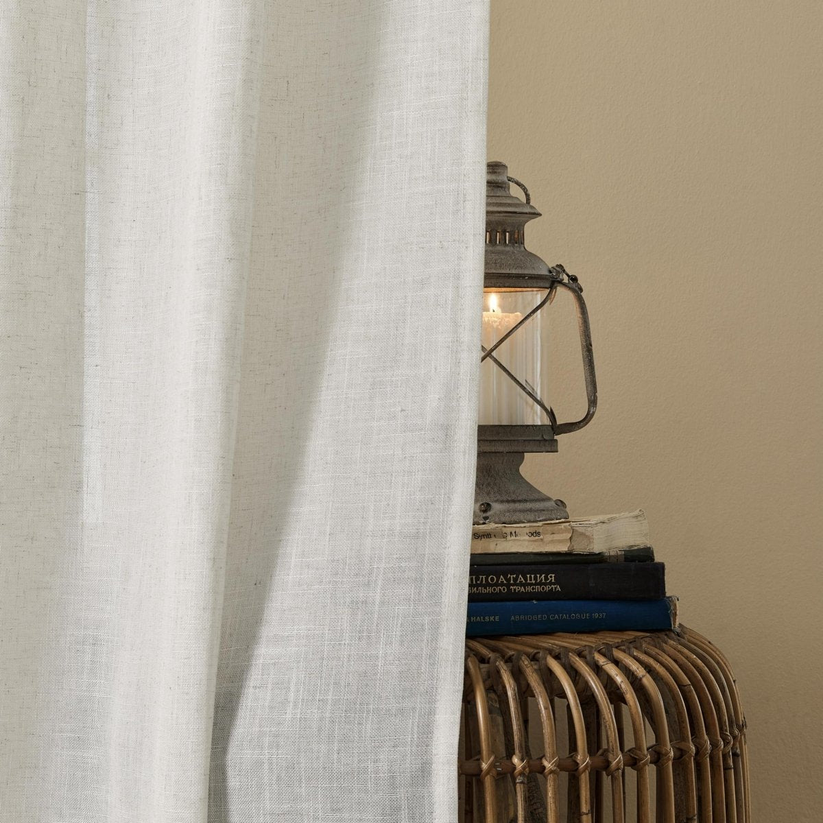 Joydeco off-white linen blend sheer curtains drape elegantly, featuring a vintage lantern with a lit candle on books.