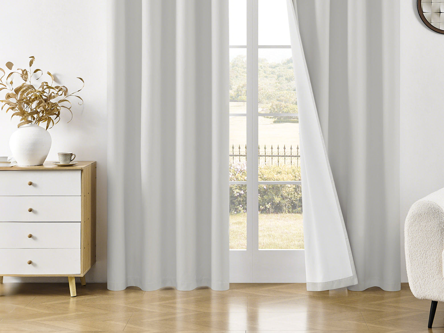 A bright room with white curtains, a wooden chest of drawers, and a scenic view through the glass door.