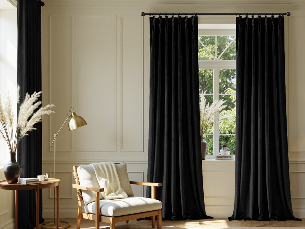 An elegant reading nook with black velvet curtains on a white paneled wall, featuring an armchair and a gold floor lamp.