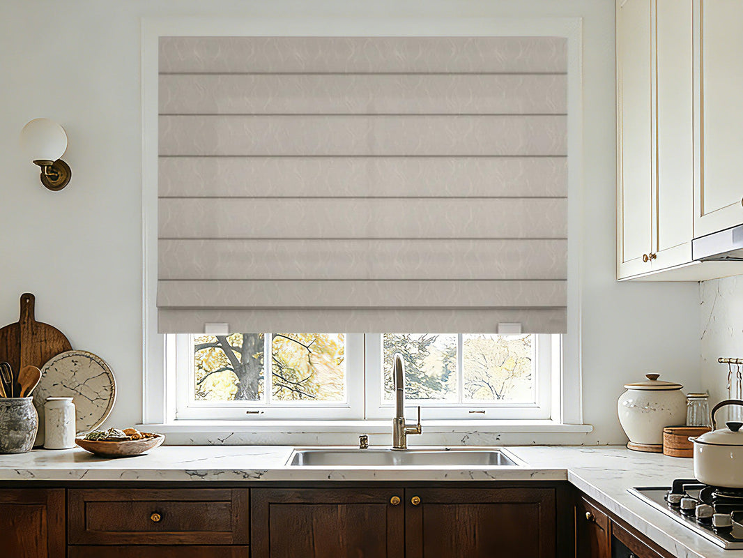 Neutral-toned Roman shade with a subtle texture covering a kitchen window above a sink and marble countertop.