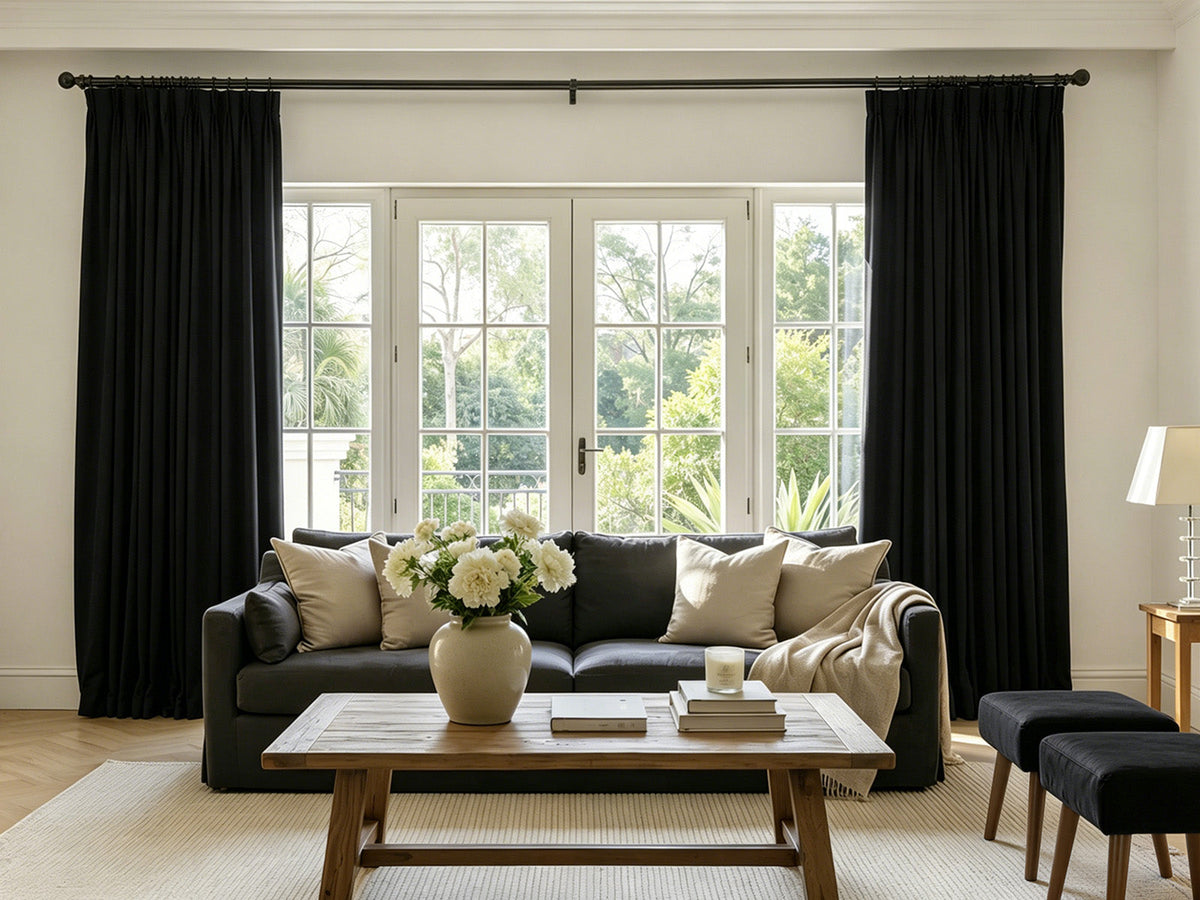 Living room with black heavy floor-to-ceiling curtains mounted wide beyond the window frame, illustrating proper full-coverage placement for noise absorption and light control
