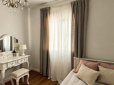 Joydeco beige panel curtains with white sheers hanging on a bedroom window.