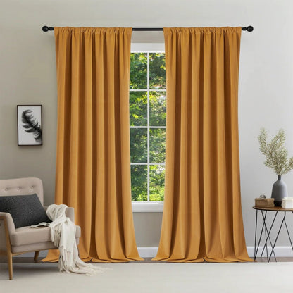 Two mustard-yellow Joydeco velvet blackout curtains on black rod, window with green trees, armchair with throw blanket.