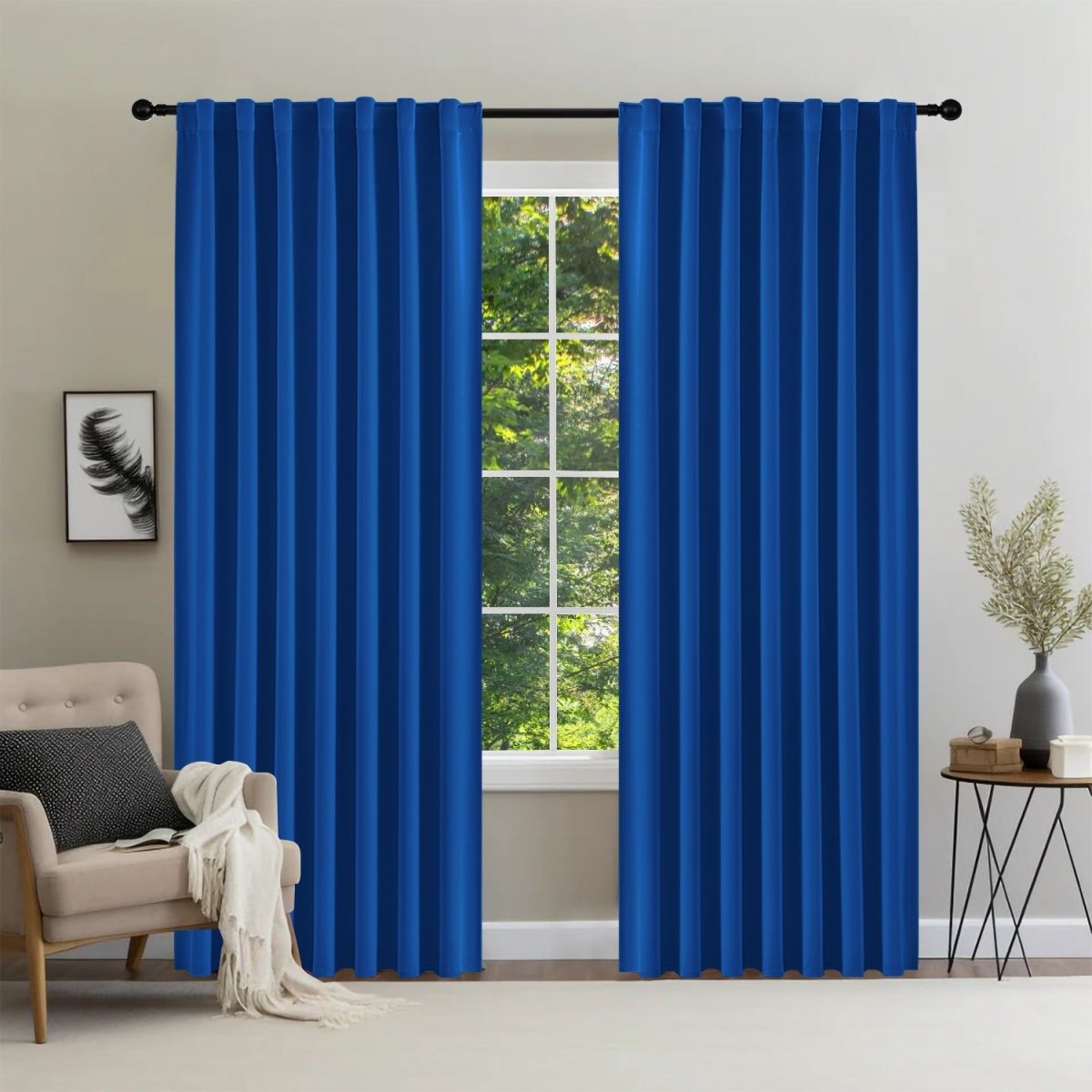 Joydeco royal blue 96 inch blackout curtains with back tabs on a window, paired with a chair and side table in a bedroom.