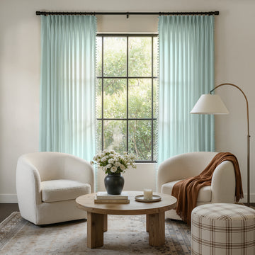 Custom light blue geometric sheer curtains with pom-pom trim in a modern boho living room.