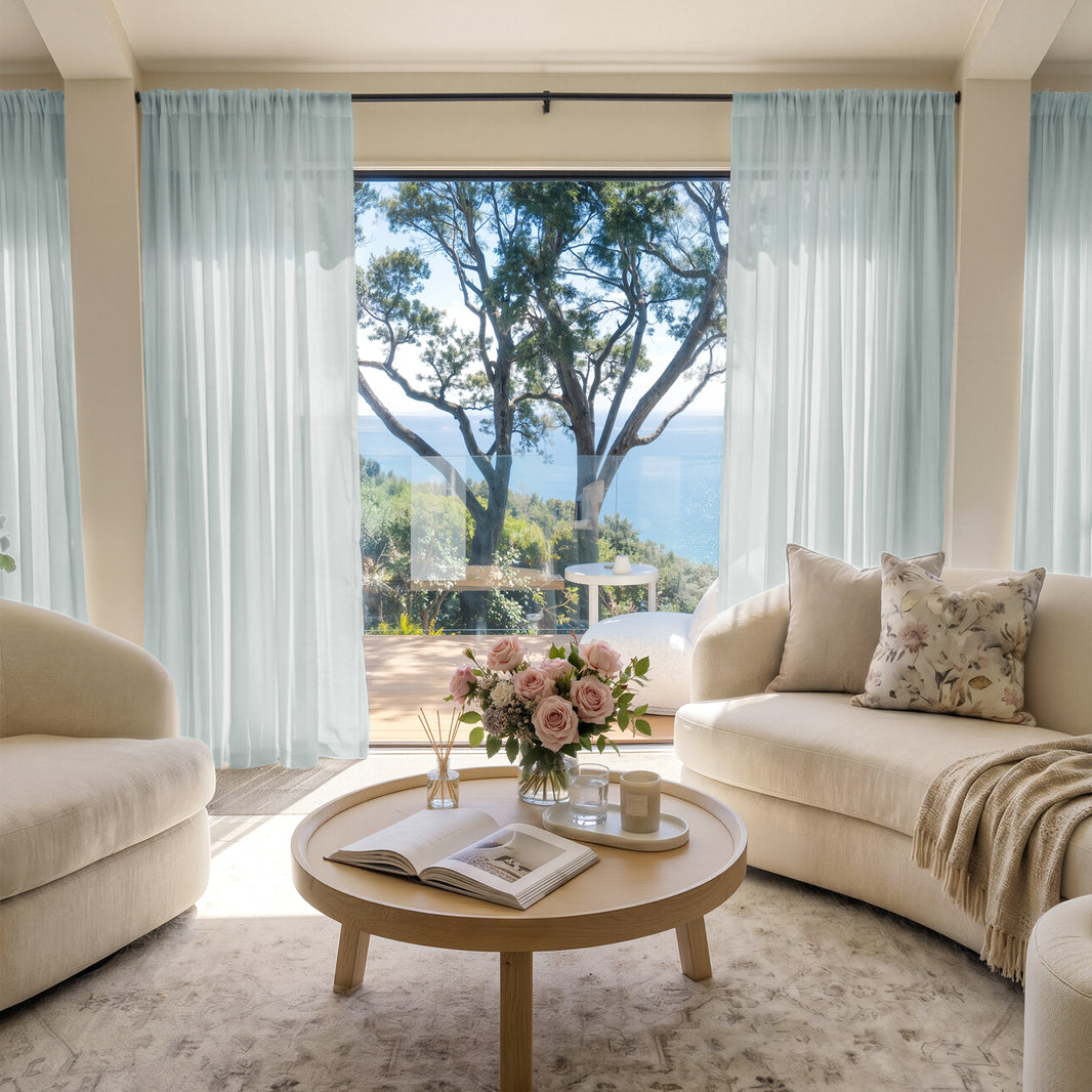 Light blue custom sheer curtains softly filter sunlight in a living room with ocean view.