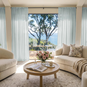 Light blue custom sheer curtains softly filter sunlight in a living room with ocean view.