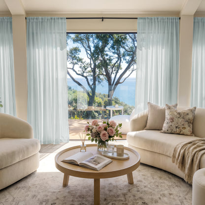 Light blue custom sheer curtains softly filter sunlight in a living room with ocean view.