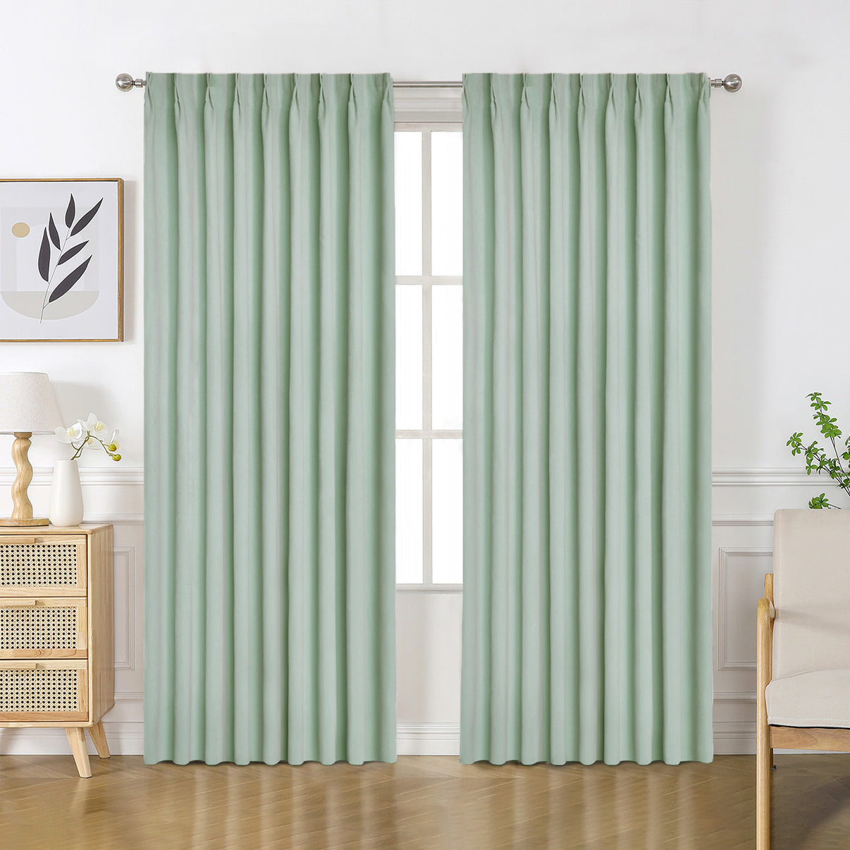 Light sage green velourette chenille blackout curtains with solid pattern and pinch pleat tops hanging in a room.