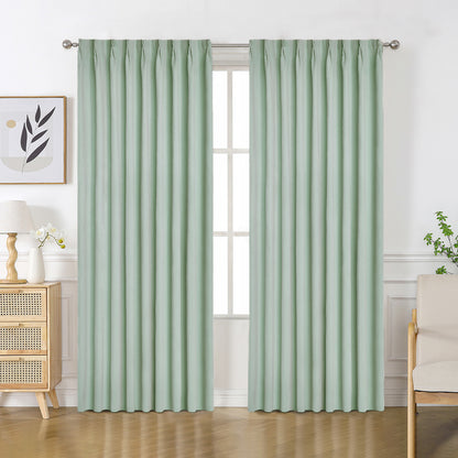 Light sage green velourette chenille blackout curtains with solid pattern and pinch pleat tops hanging in a room.