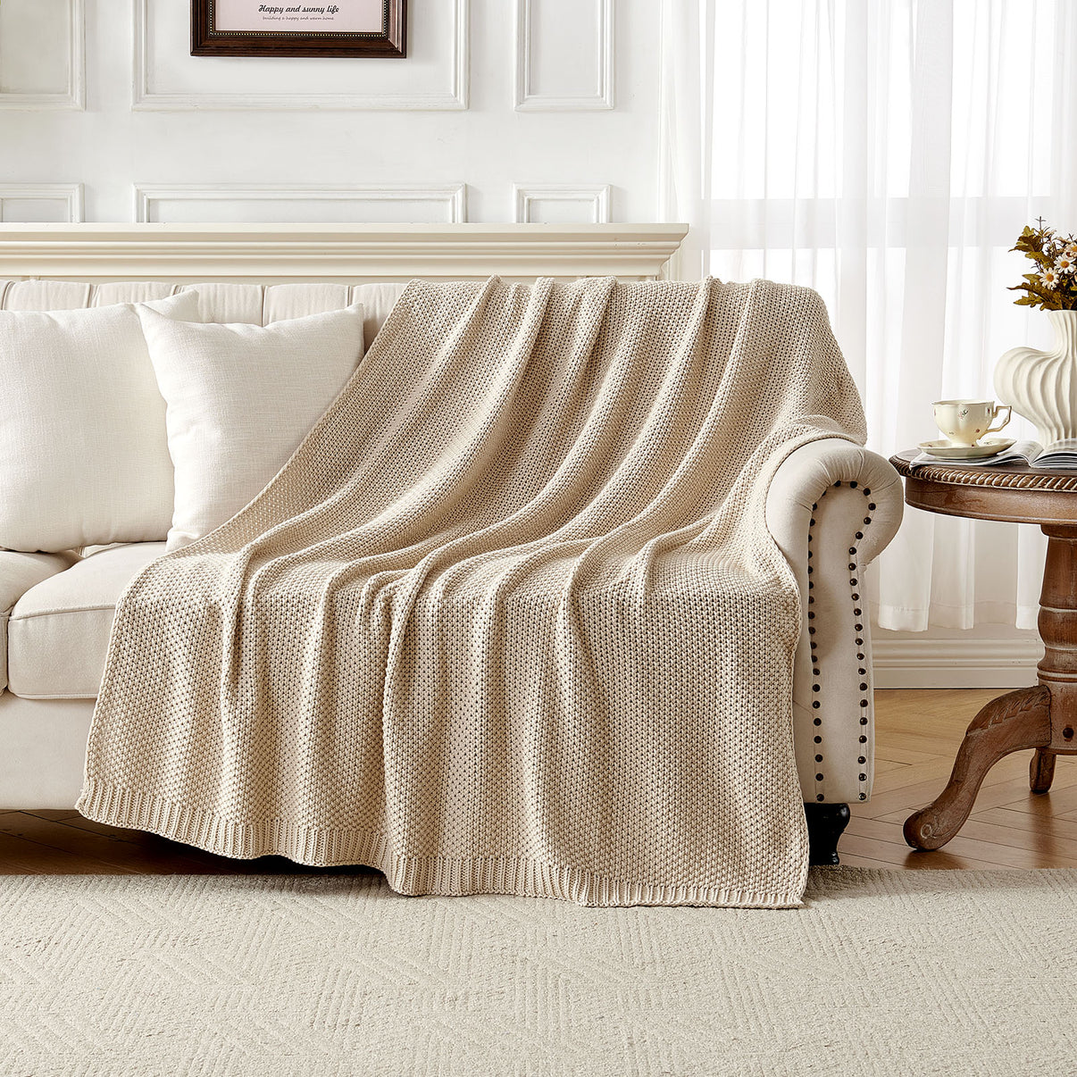 Light beige 100% cotton cable knit throw blanket draped over a cream sofa, showcasing cozy texture for farmhouse decor.