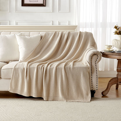 Light beige 100% cotton cable knit throw blanket draped over a cream sofa, showcasing cozy texture for farmhouse decor.