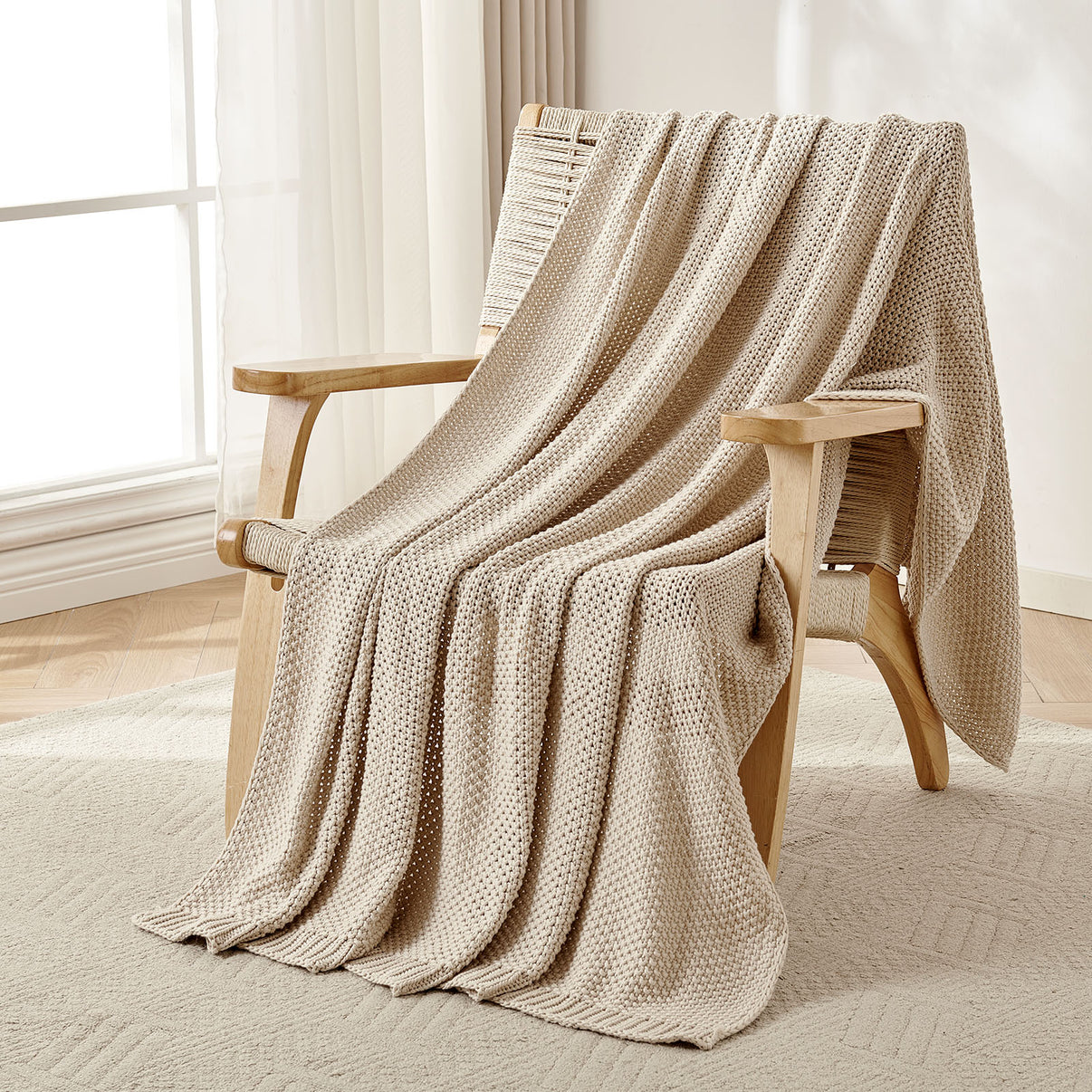 Beige chunky knit cotton throw blanket draped over a wooden armchair, showcasing farmhouse texture and coziness.