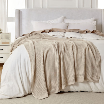 Light beige 100% cotton chunky knit throw blanket with textured pattern on a white bed. Farmhouse style.