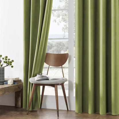 Two moss green velvet blackout curtains with rich texture, near a chair by a window.