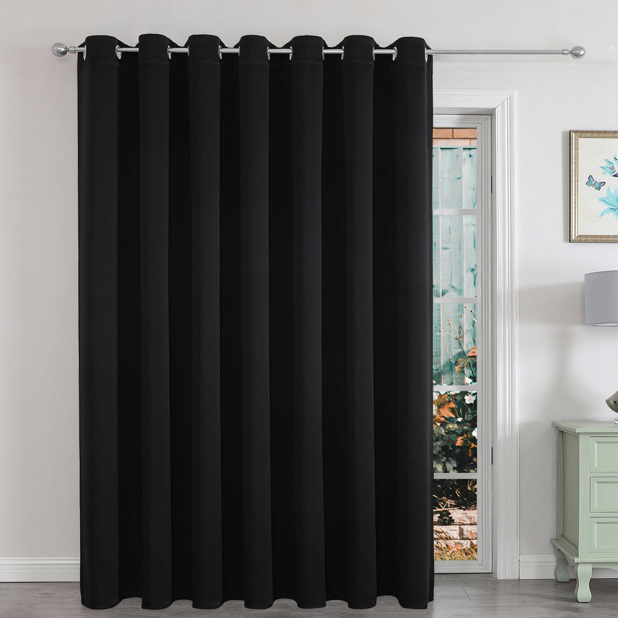 Black extra-wide blackout curtain panel for sliding glass door in a living room, providing privacy and light control.