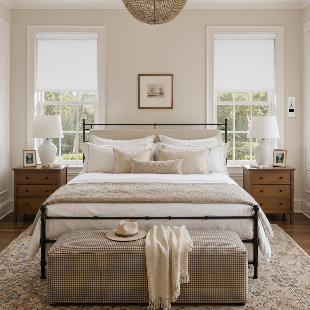 White motorized blackout roller shades in a beige bedroom, fully lowering over windows
