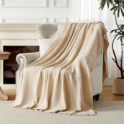 Joydeco 4-layer cotton muslin throw blanket, light beige, draped on armchair. Cozy gauze texture, living room scene.