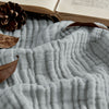 Light blue 4-layer cotton muslin throw blanket texture, with natural decor elements.