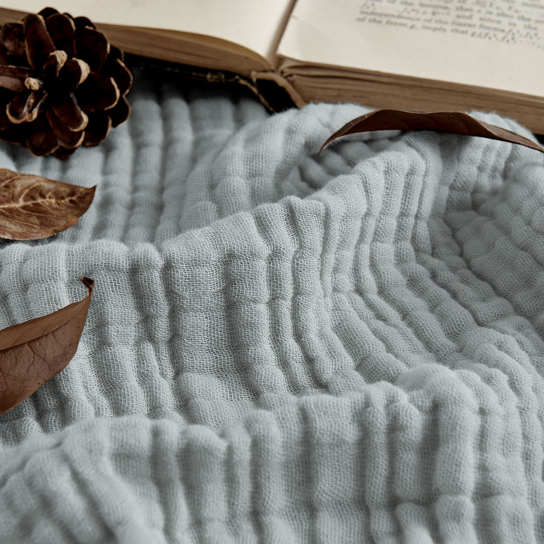 Light blue 4-layer cotton muslin throw blanket texture, with natural decor elements.