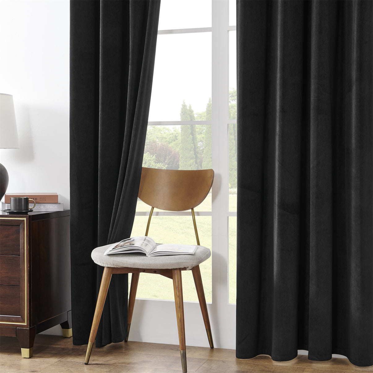 Black velvet blackout curtains with rod pocket, 84-inch length, in a cozy bedroom with a chair and side table.