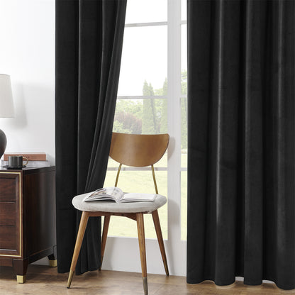 Black velvet blackout curtains with rod pocket, 84-inch length, in a cozy bedroom with a chair and side table.