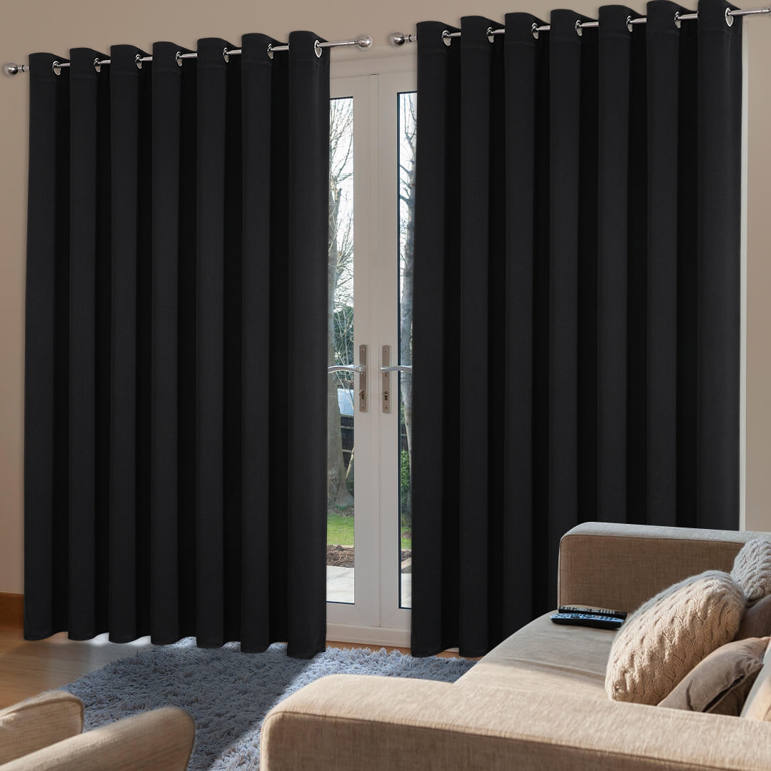 Extra wide black blackout curtains cover sliding glass doors in a living room, blocking light and providing privacy.