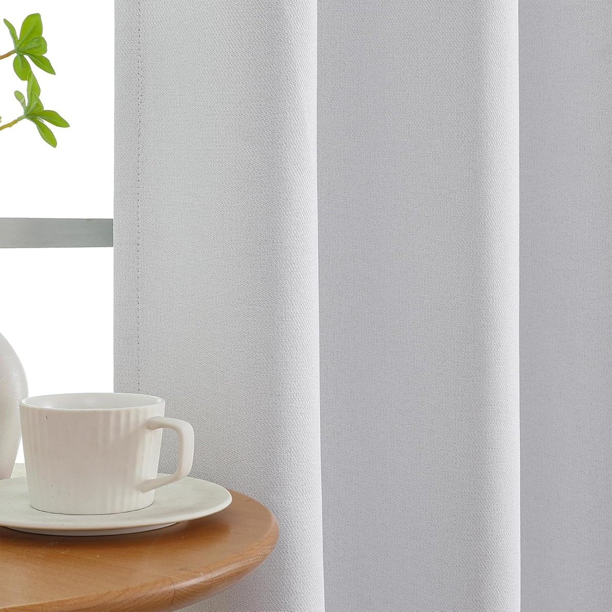Close-up of light gray faux linen blackout curtain showing woven texture and stitching detail, with mug on side table.
