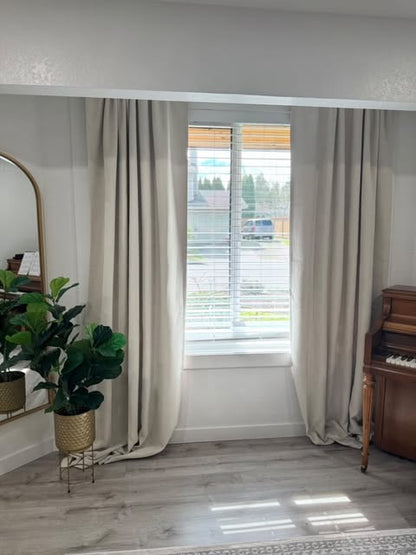 Two beige Joydeco 100% blackout velvet curtains hanging on a window, with blinds, plant and piano in room.