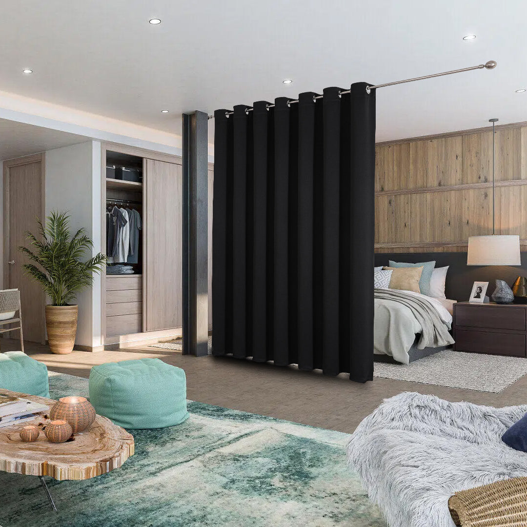 Black extra wide blackout curtain used as a room divider in a studio apartment, separating bedroom from living area.