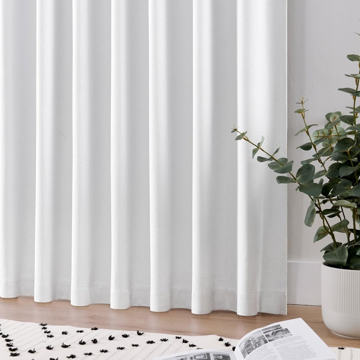 Joydeco white blackout curtains with brushed texture and vertical pleats shown in a living room with a potted plant.