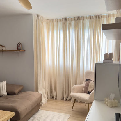 Off-white Joydeco linen blend semi-sheer curtains filtering light in a modern living room with armchair and sofa.
