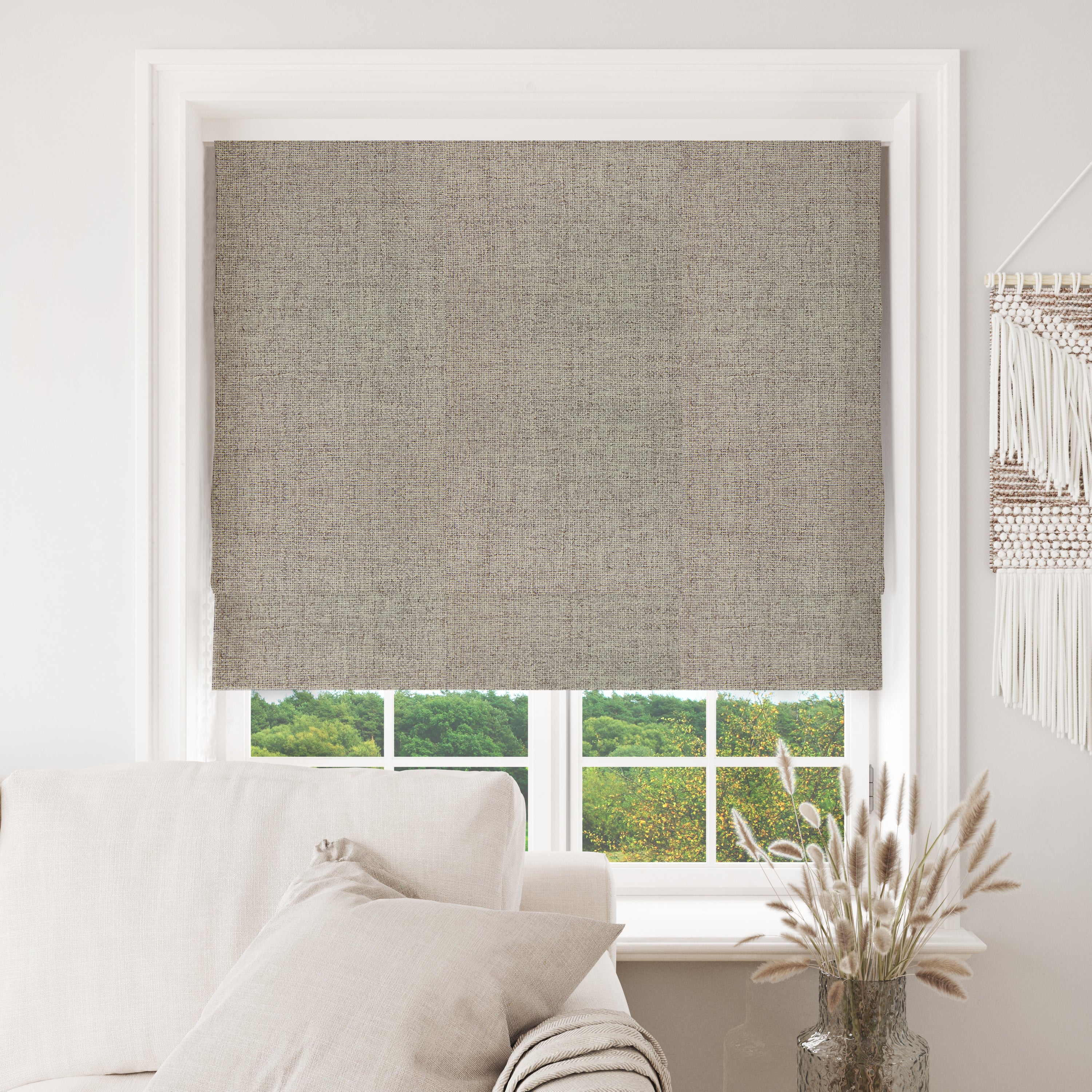Joydeco greige blackout Roman shade with linen texture in white window, over sofa and greenery view.