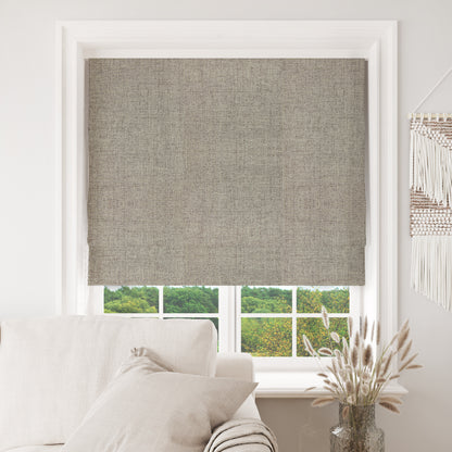 Joydeco greige blackout Roman shade with linen texture in white window, over sofa and greenery view.