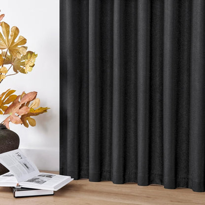Black faux linen blackout drapes with elegant vertical pleats, set in a cozy living room with decorative leaves and books.